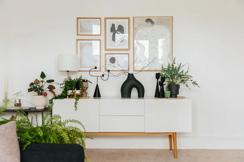 Living room sideboard styled with a framed gallery wall, plants and black vases by My Bespoke Room