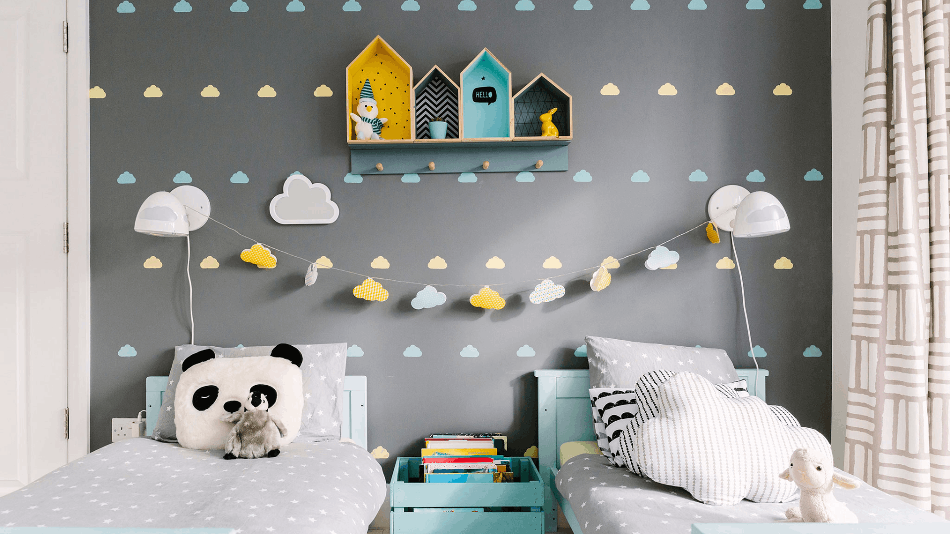 Shared children’s bedroom with two single beds, cloud-patterned wallpaper, and book storage between the beds.