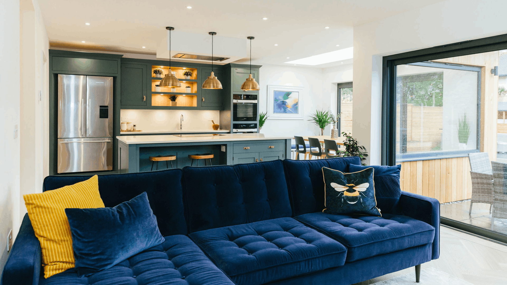 Open-plan kitchen and living room separated into zones by a navy blue sofa.