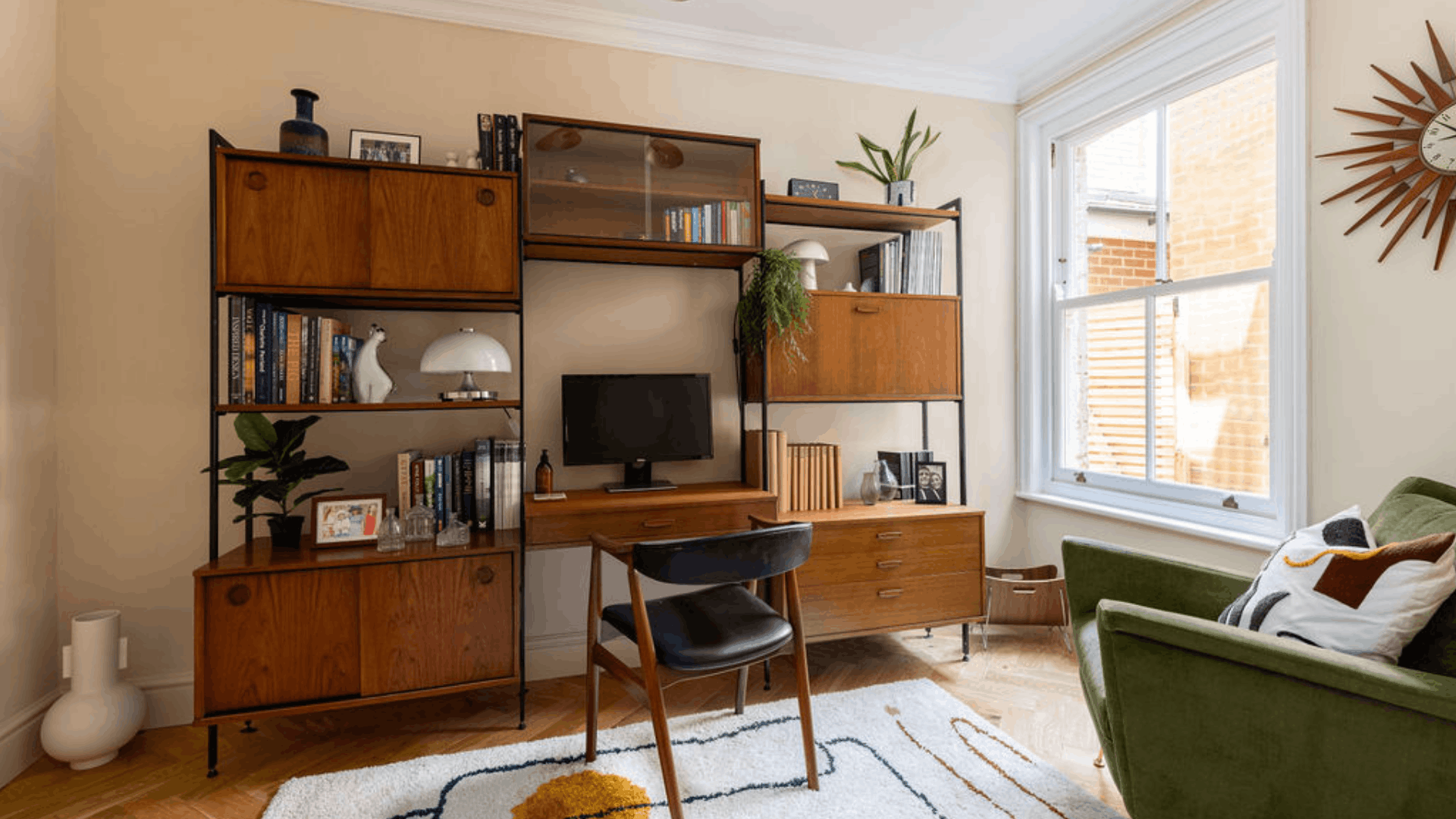 Mid-century home office with a wooden wall unit, computer monitor, books and a green armchair.