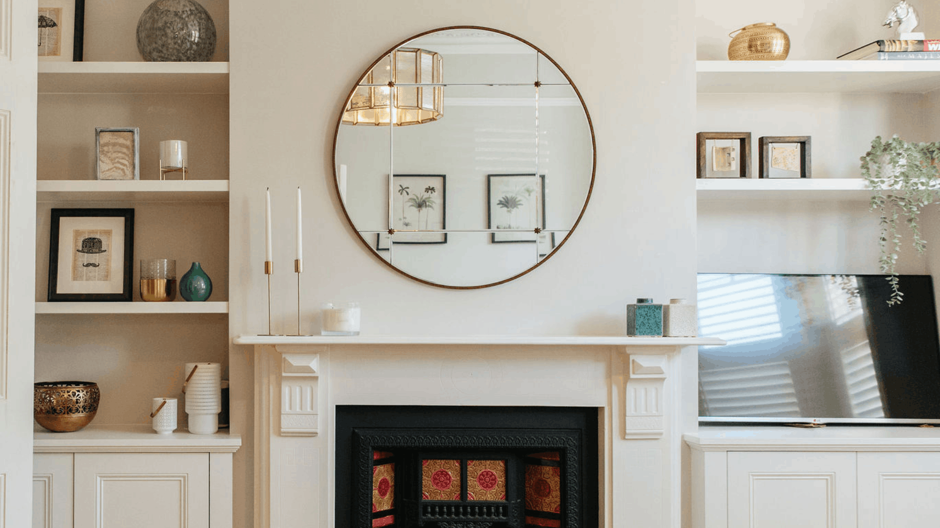 Neutral living room with a large round mirror above a fireplace and alcove shelves.
