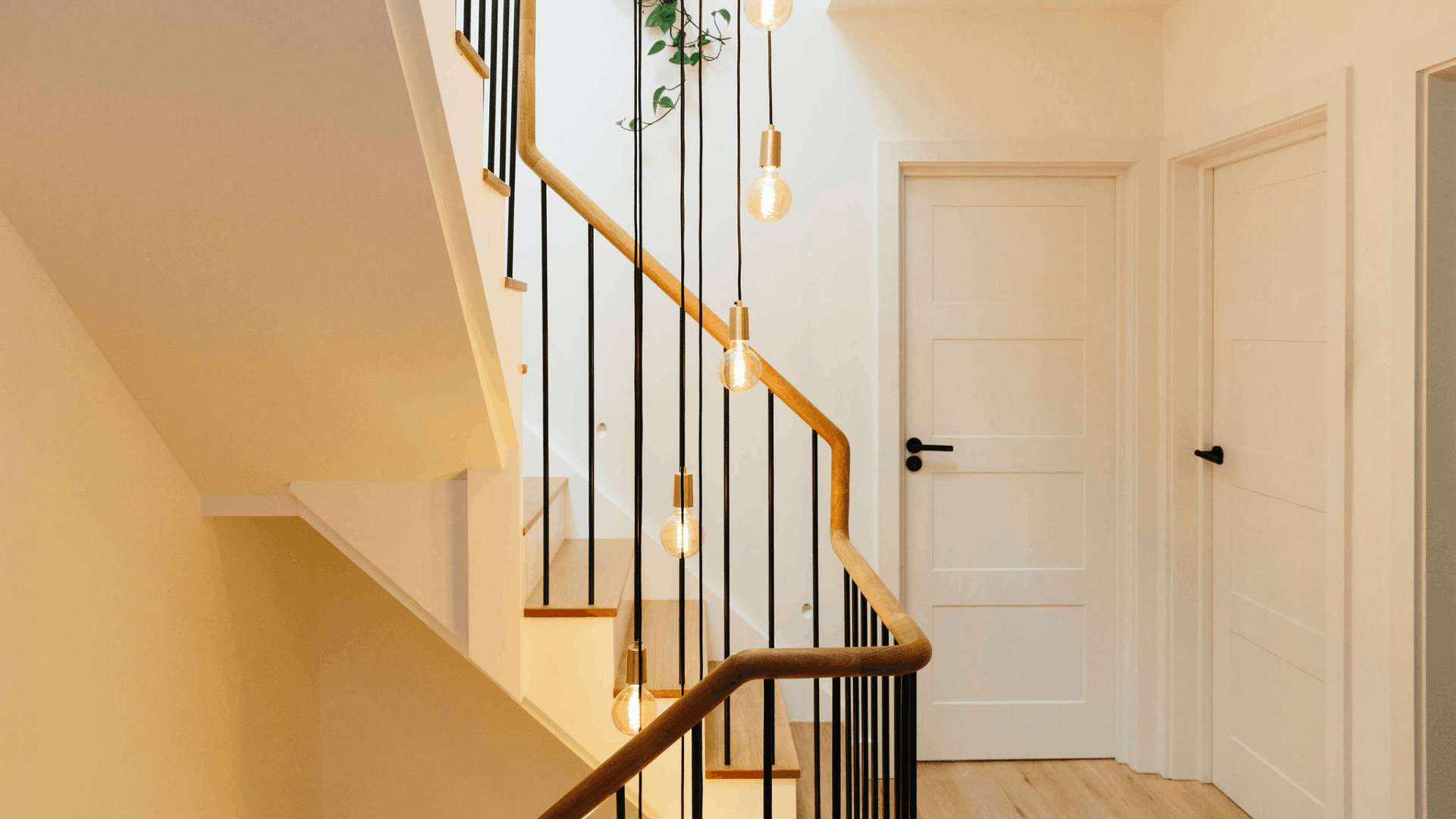 Modern staircase with wooden handrails, black metal balustrades and hanging pendant lights in a bright hallway.
