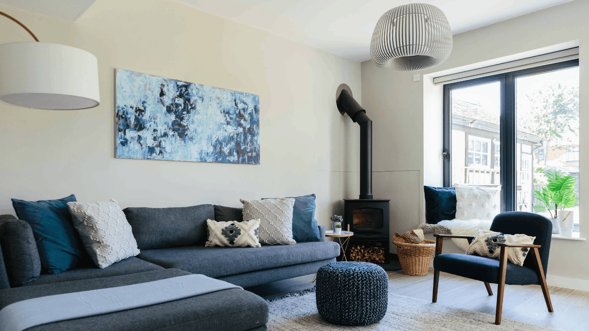 Bright, open plan living room with a blue corner sofa, fireplace, dark blue armchair and a window seat.