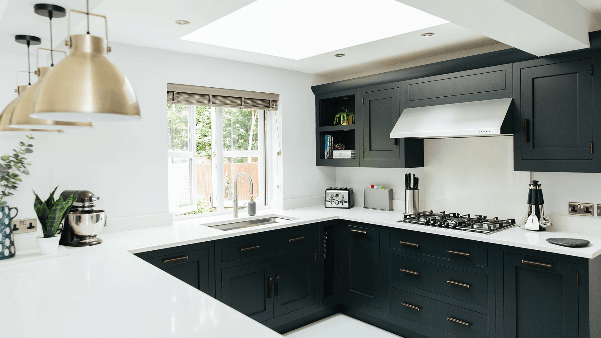 Bright kitchen with white countertops, black cabinetry, a skylight, pendant island lighting and an open window with bamboo blinds.